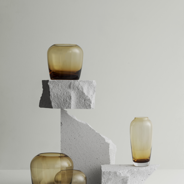 Elegant amber glass vases displayed on textured stone pedestals against a minimalist backdrop.