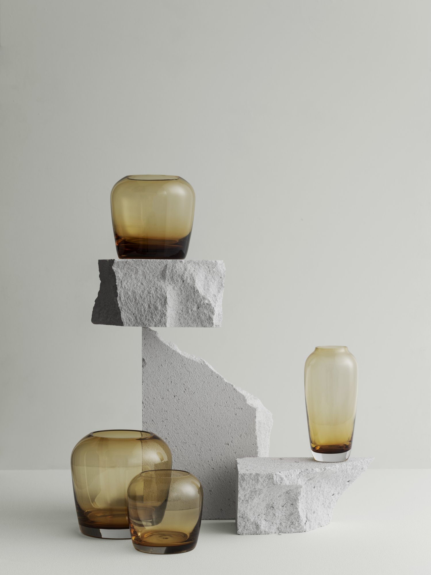 Elegant amber glass vases displayed on textured stone pedestals against a minimalist backdrop.