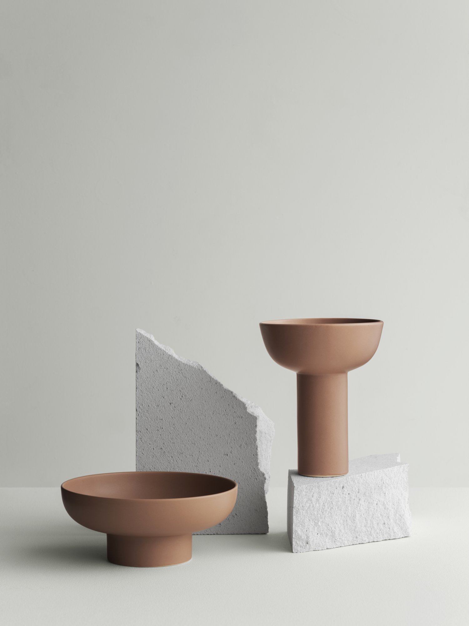 Minimalistische Keramikschalen, die auf strukturierten Steinoberflächen vor einem sanften grauen Hintergrund präsentiert werden.