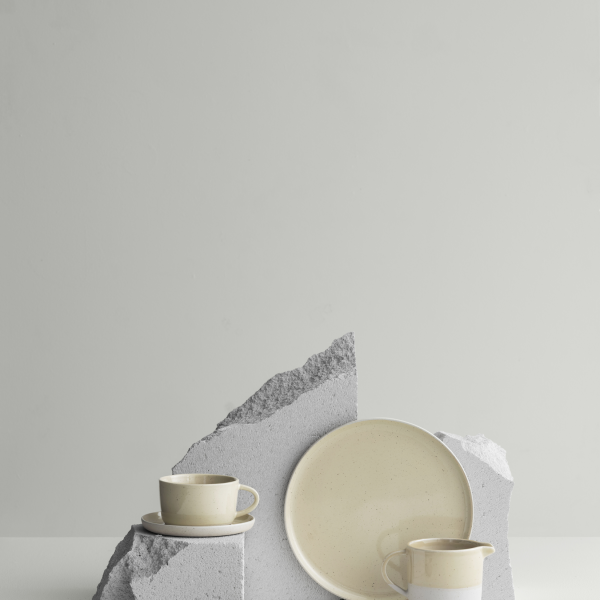 Stylish minimalistic table setting with ceramic cups and a plate on gray stone display.