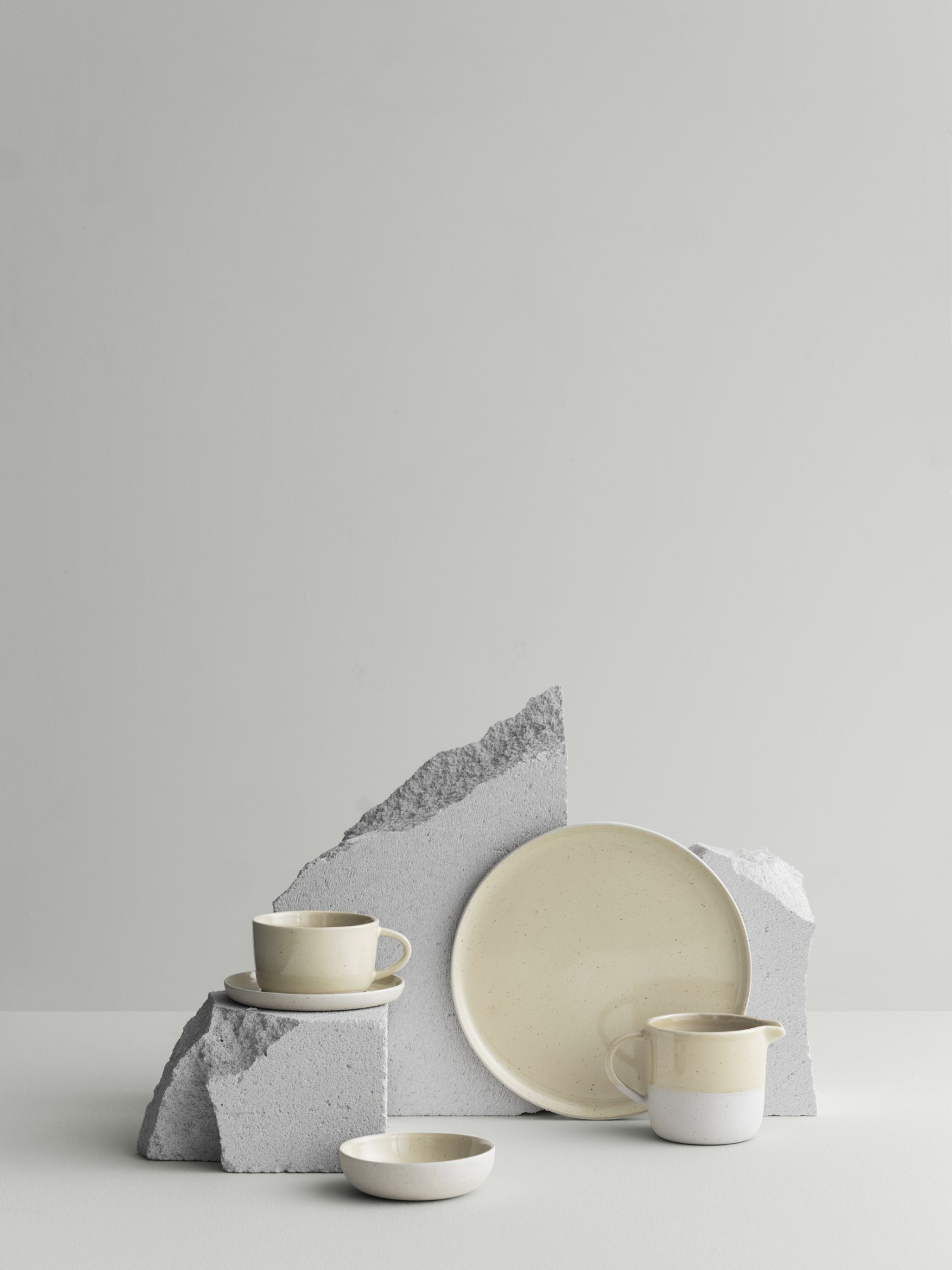 Stylish minimalistic table setting with ceramic cups and a plate on gray stone display.