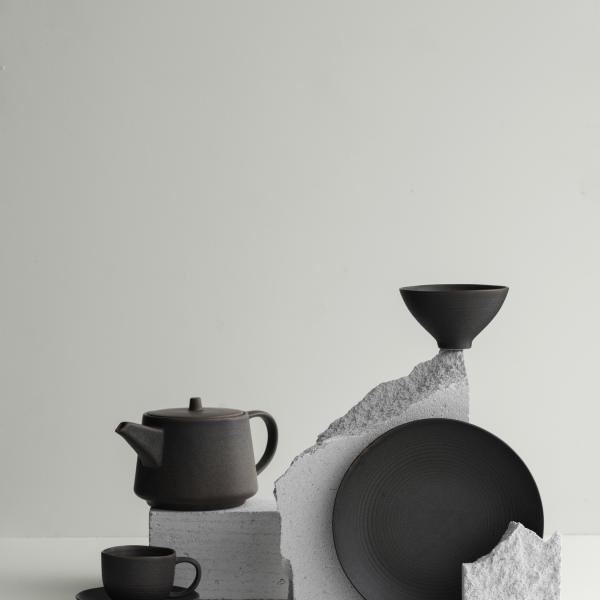 Moderne schwarze Keramik, präsentiert mit strukturierten Steinelementen vor einem minimalistischen Hintergrund.