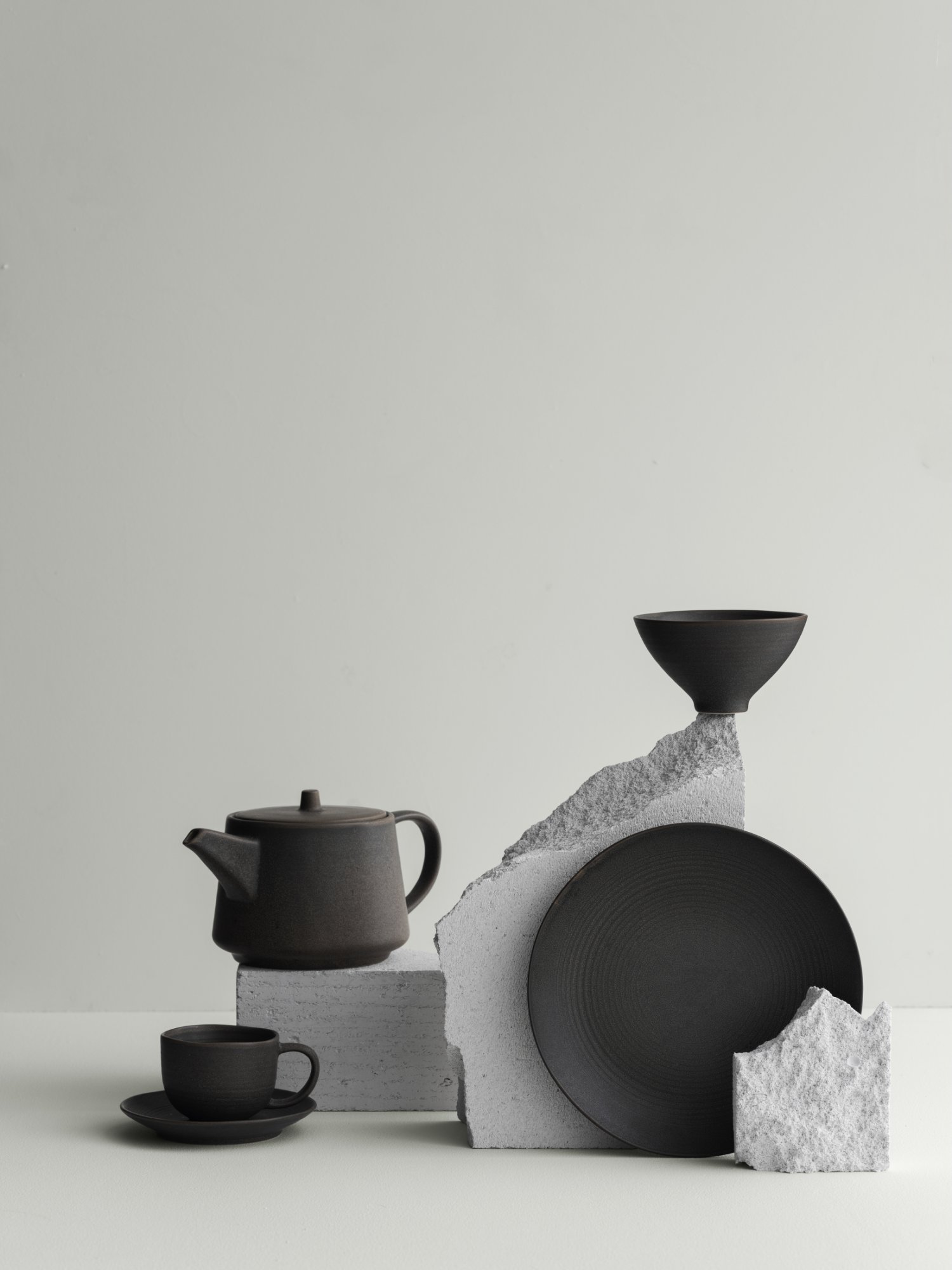 Moderne schwarze Keramik, präsentiert mit strukturierten Steinelementen vor einem minimalistischen Hintergrund.
