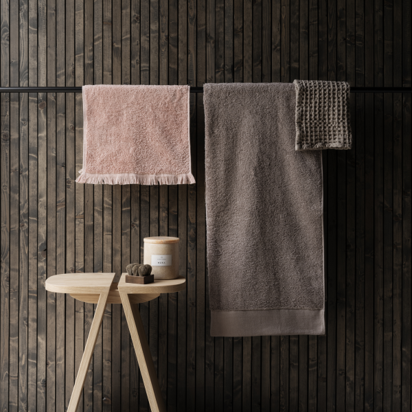 Soft pink and grey towels hanging on a rustic wooden rack next to a candle on a side table.