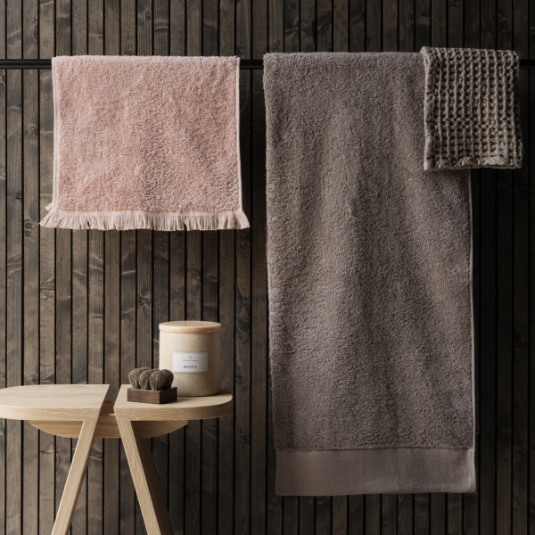 Soft, plush towels in neutral tones hanging on a wooden wall with a decorative stool.