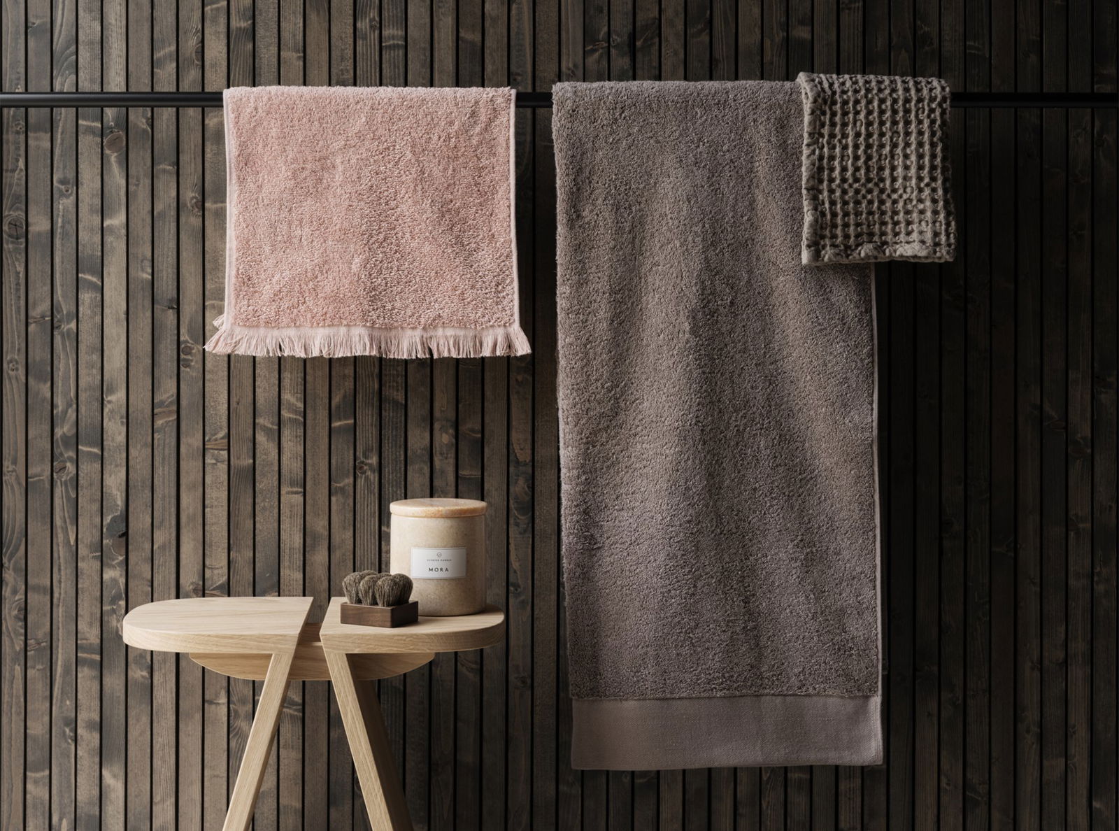 Soft, plush towels in neutral tones hanging on a wooden wall with a decorative stool.