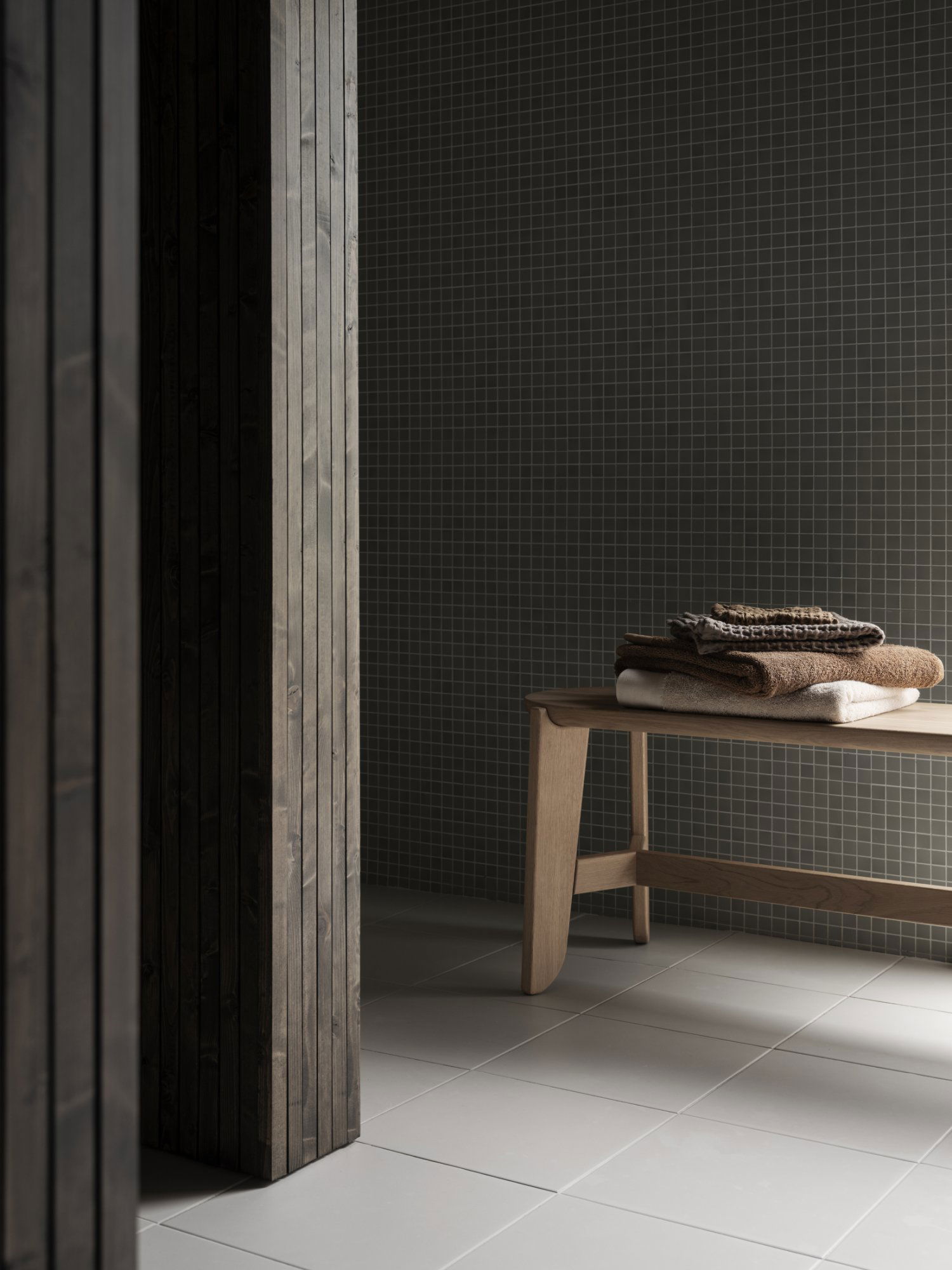 A minimalist bathroom scene featuring a wooden bench with neatly stacked towels.