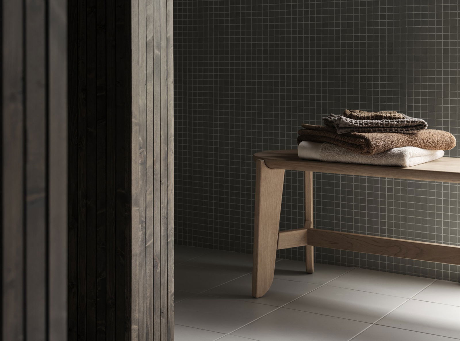 Minimalist bathroom featuring wooden bench with neatly stacked towels against a textured wall.