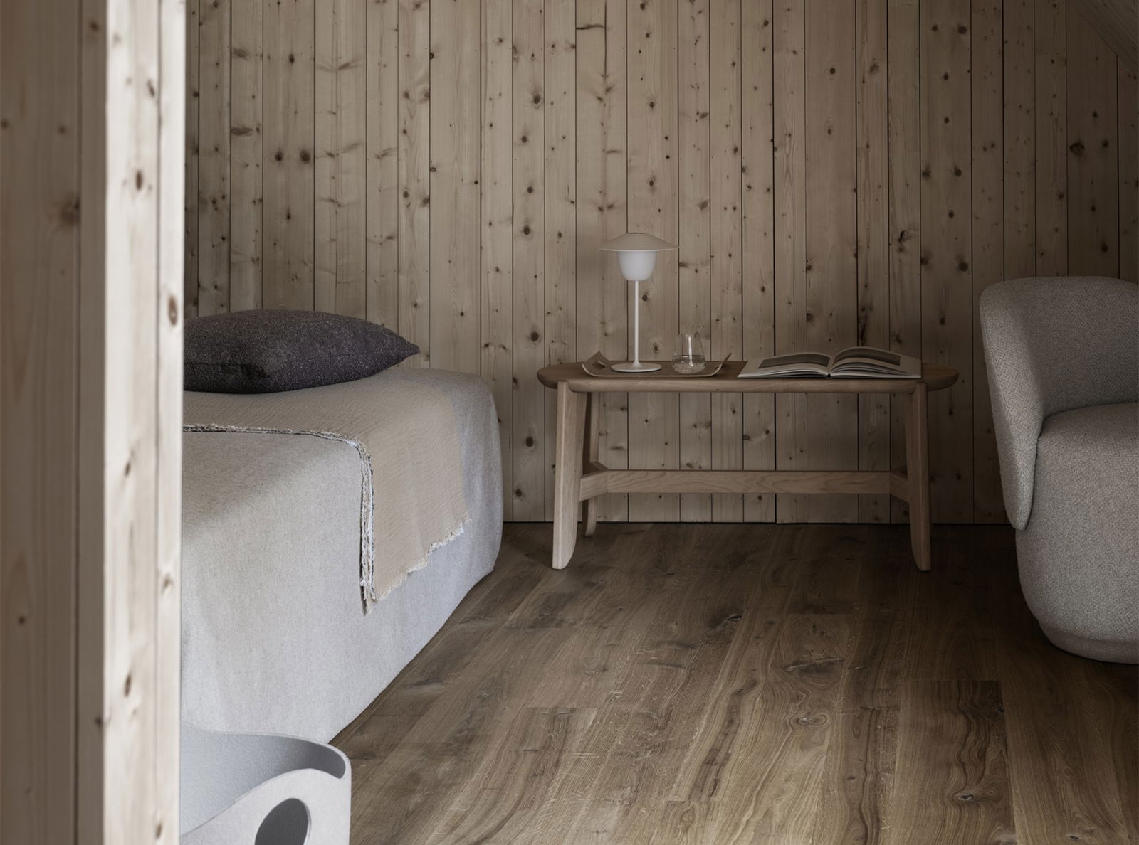 Gemütlicher Holzraum mit einem Bett, Tisch, Lampe und minimalistischer Dekoration.