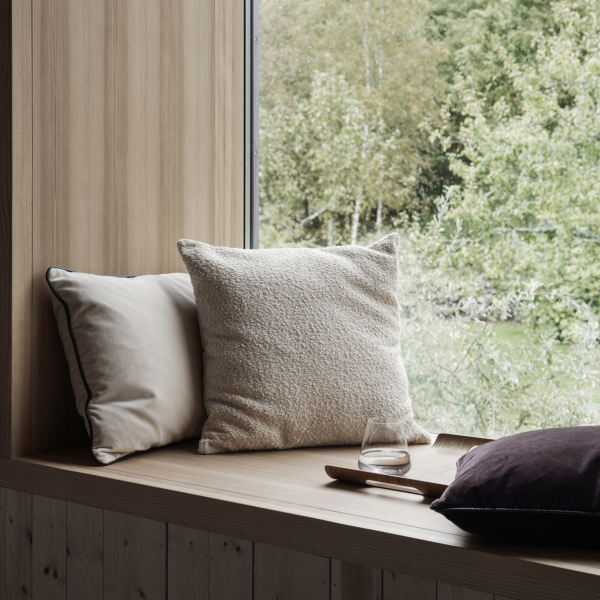 Gemütlicher Fenstersitz mit weichen Kissen und einem Glas auf einem Holzregal mit Blick auf die Natur.