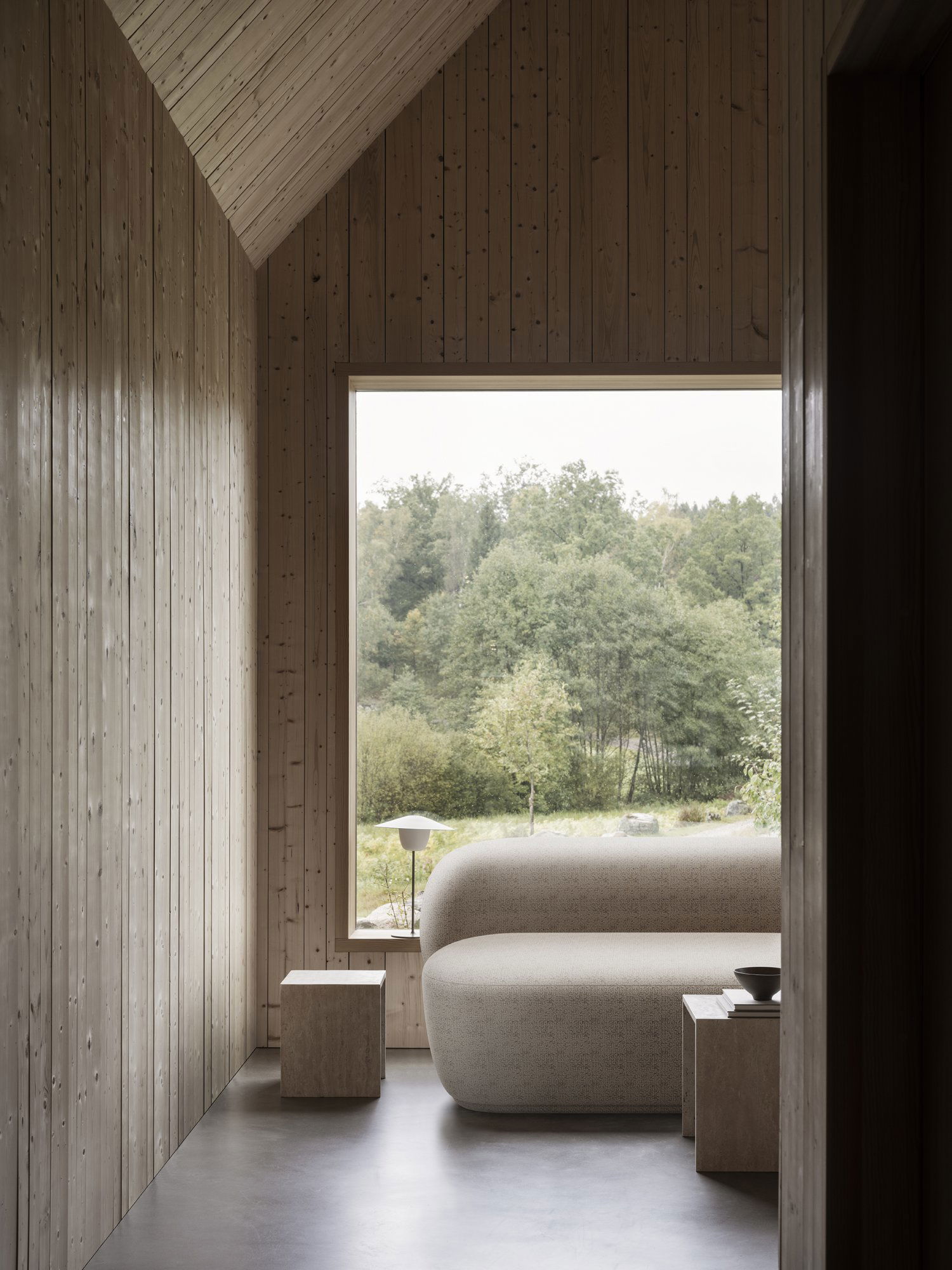 Cozy interior with a modern sofa and large window overlooking a serene nature view.