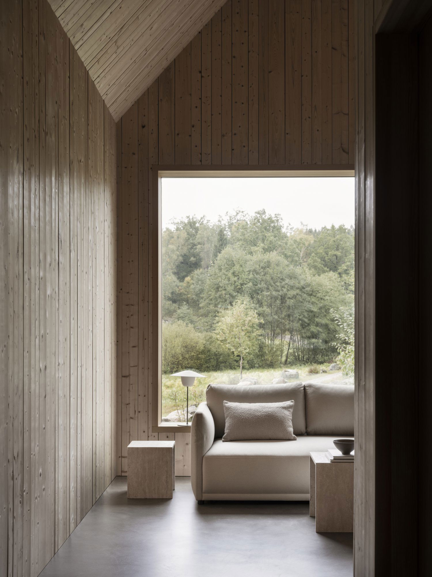Gemütliches Interieur mit einem minimalistischen Sofa und einem malerischen Blick auf die Natur durch ein großes Fenster.