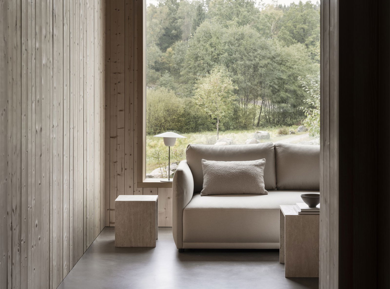 Modern interior with a cozy sofa and natural scenery visible through large windows.