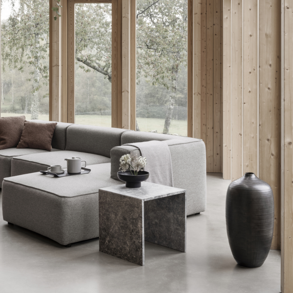 Modernes Wohnzimmer mit gemütlicher grauer Couch, marmoriertem Beistelltisch und stilvollen Vasen in einer natürlichen Umgebung.
