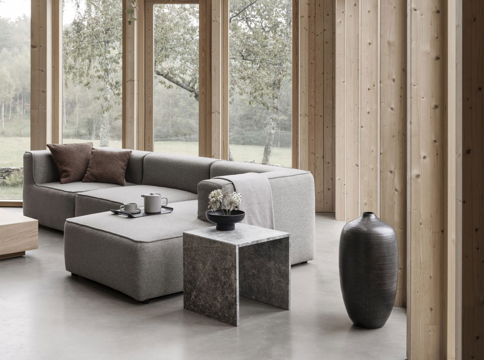 Modernes Wohnzimmer mit gemütlicher grauer Couch, marmoriertem Beistelltisch und stilvollen Vasen in einer natürlichen Umgebung.