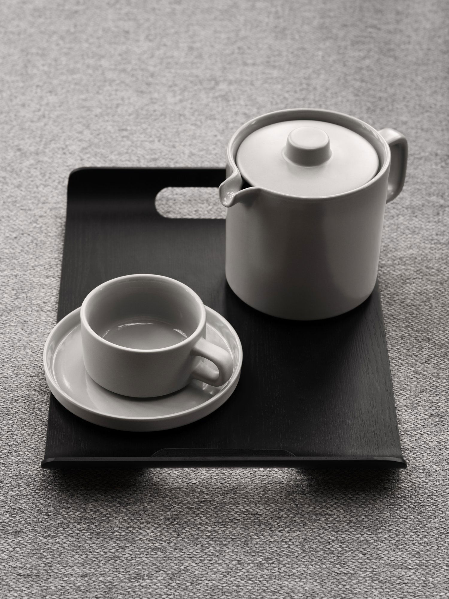 Elegantes Teeset auf einem schwarzen Tablett mit einer Teekanne, einer Tasse und einer Untertasse im minimalistischen Design.
