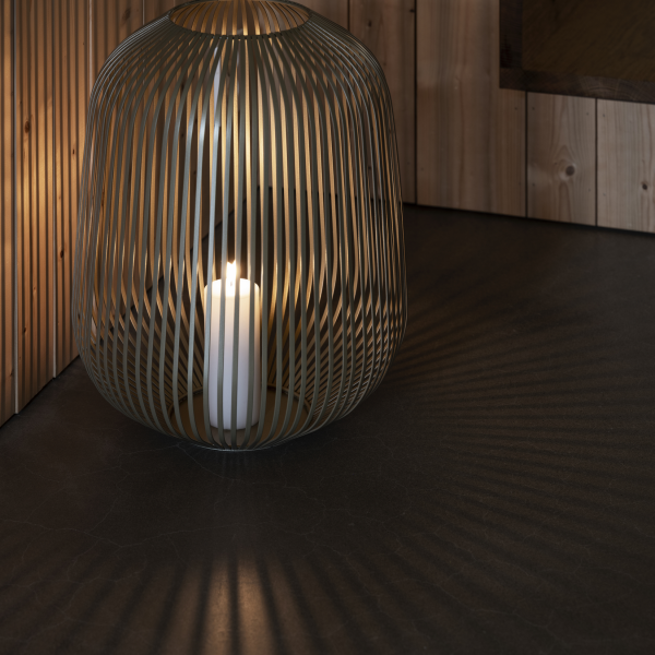 Stylische offen gewebte Lampe, die Schatten wirft, mit einer Kerze im Inneren in einer gemütlichen Inneneinrichtung.