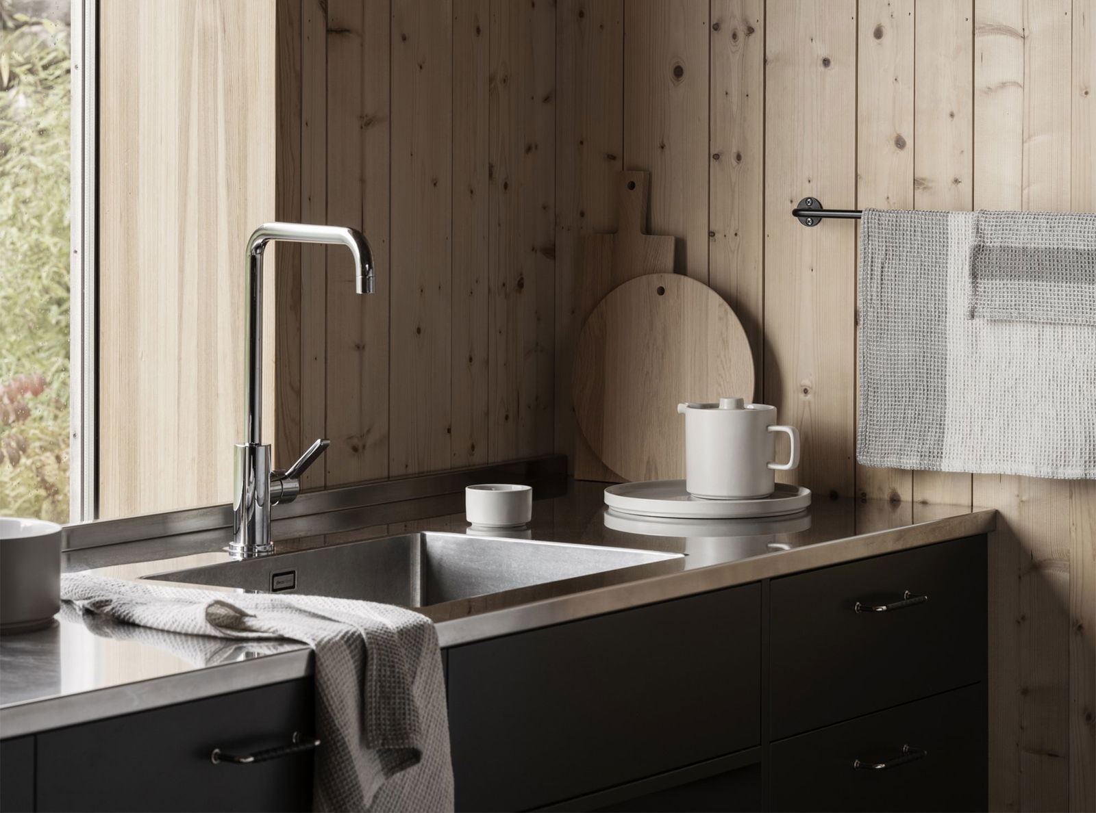 Modern kitchen with wooden walls, stainless steel sink, and minimalist dishware.