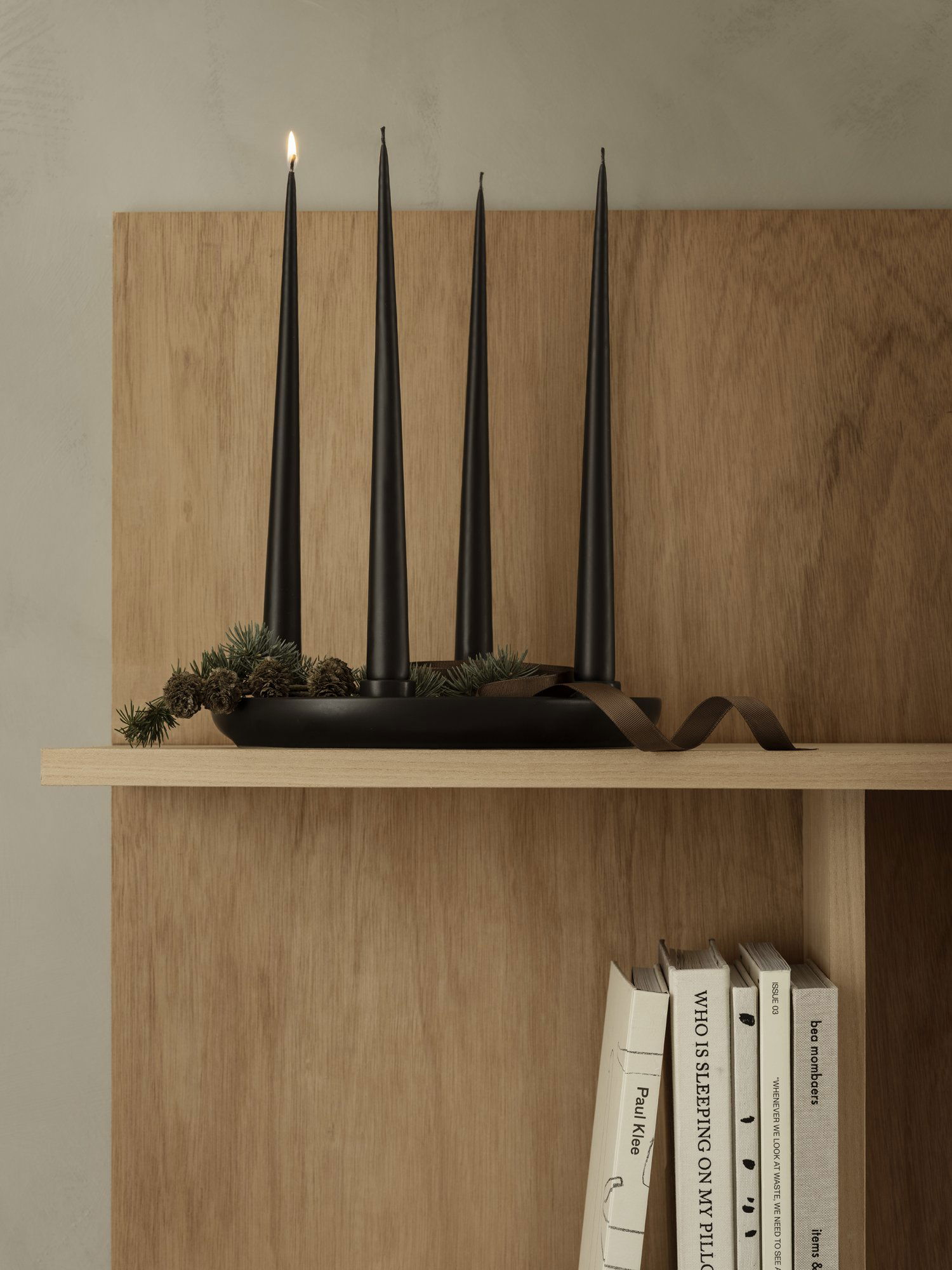 Elegante schwarze Kerzenständer auf einem Holzregal mit natürlichen Akzenten und Büchern.