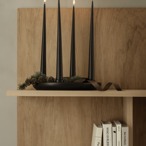 Stylische Regalpräsentation mit schwarzen Spitzkerzen, Grünpflanzen und Büchern vor einem hölzernen Hintergrund.