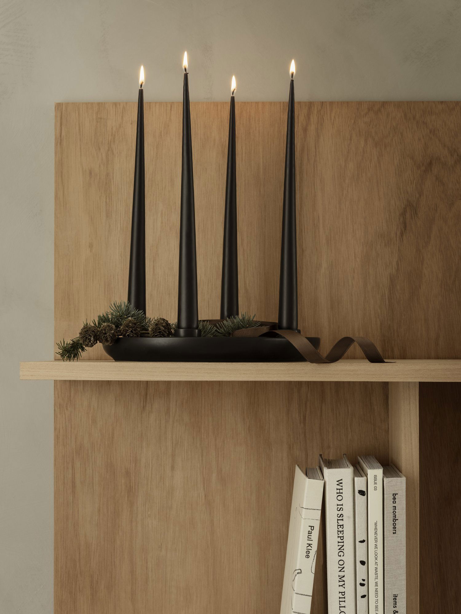 Stylische Regalpräsentation mit schwarzen Spitzkerzen, Grünpflanzen und Büchern vor einem hölzernen Hintergrund.