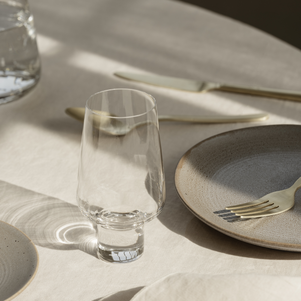 Elegant glass on a beautifully set dining table with gold cutlery and textured plates.