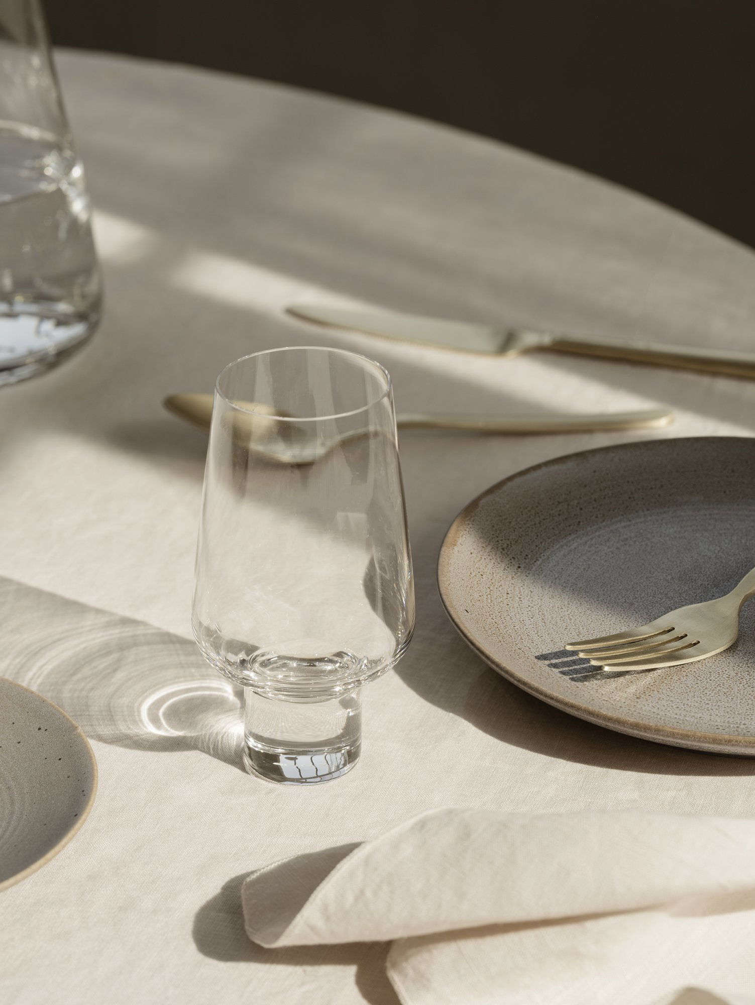 Elegant glass on a beautifully set dining table with gold cutlery and textured plates.