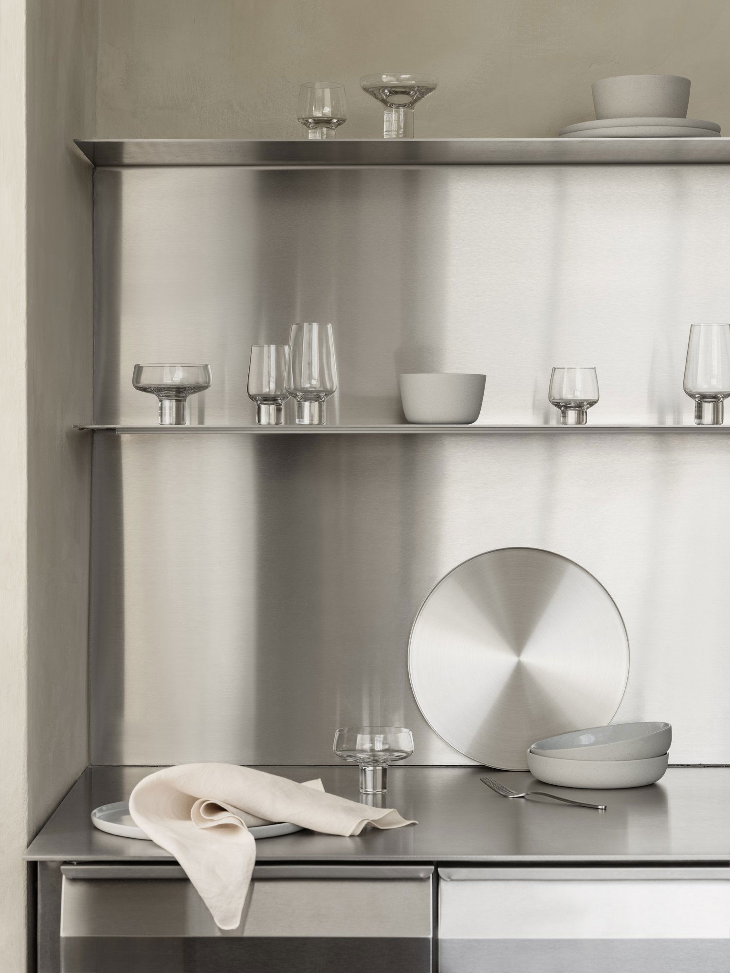 Modern stainless steel kitchen shelves displaying elegant glassware and ceramic dishes.