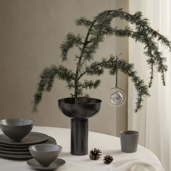 Moderne Tischdekoration mit einer eleganten schwarzen Vase, einem Fichtenzweig und dekorativen Ornamenten.