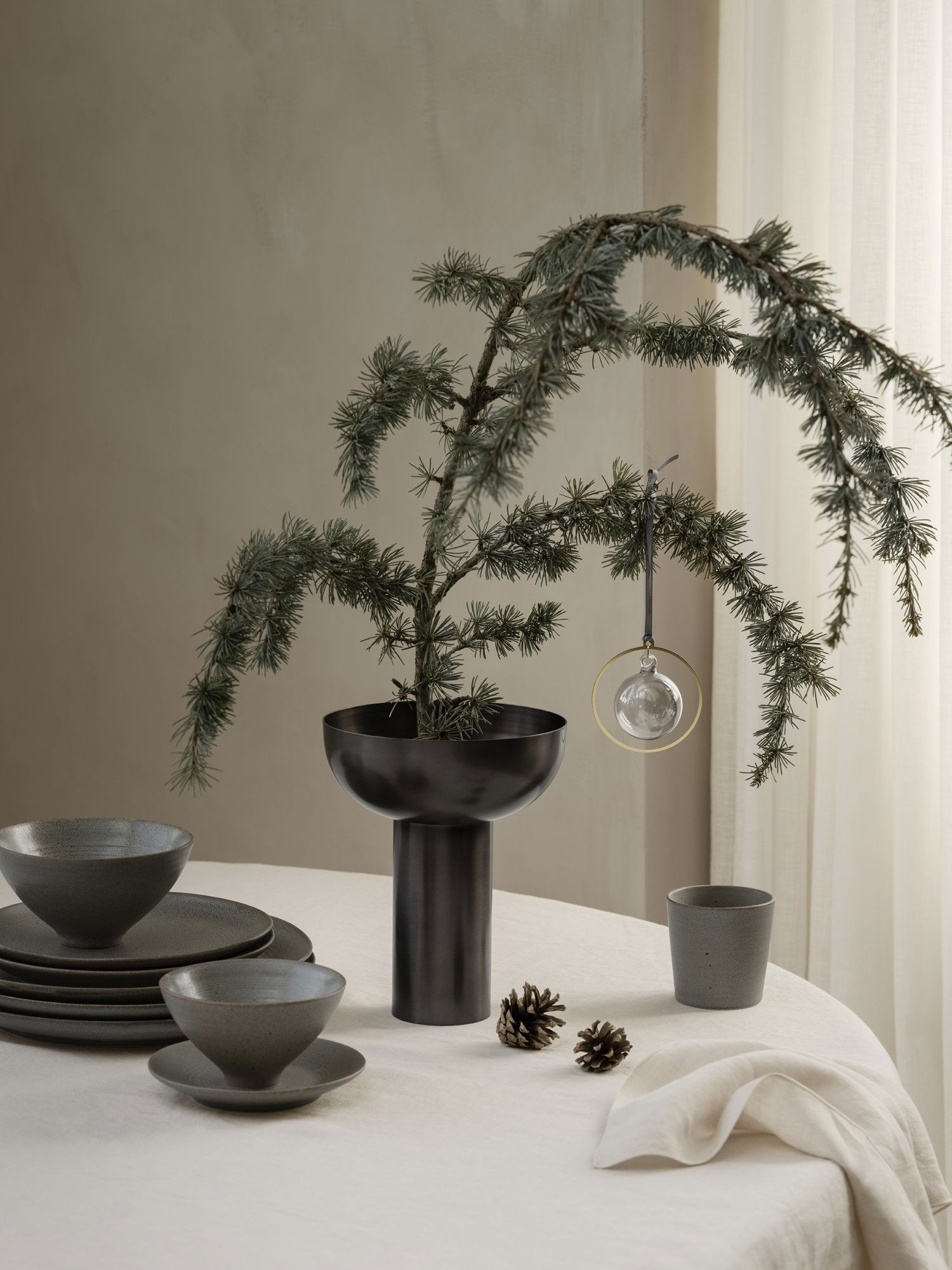 Moderne Tischdekoration mit einer eleganten schwarzen Vase, einem Fichtenzweig und dekorativen Ornamenten.
