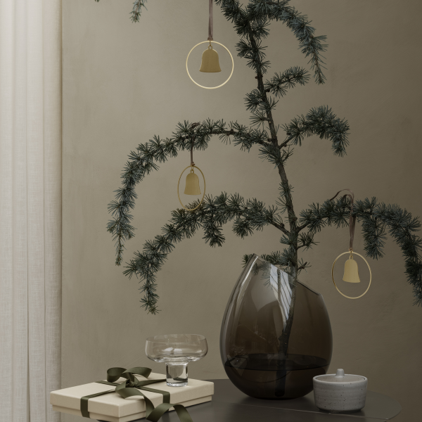 Elegante Weihnachtsdekoration mit einem grünen Baum, goldenen Glocken und einem Geschenk auf einem stilvollen Tisch.