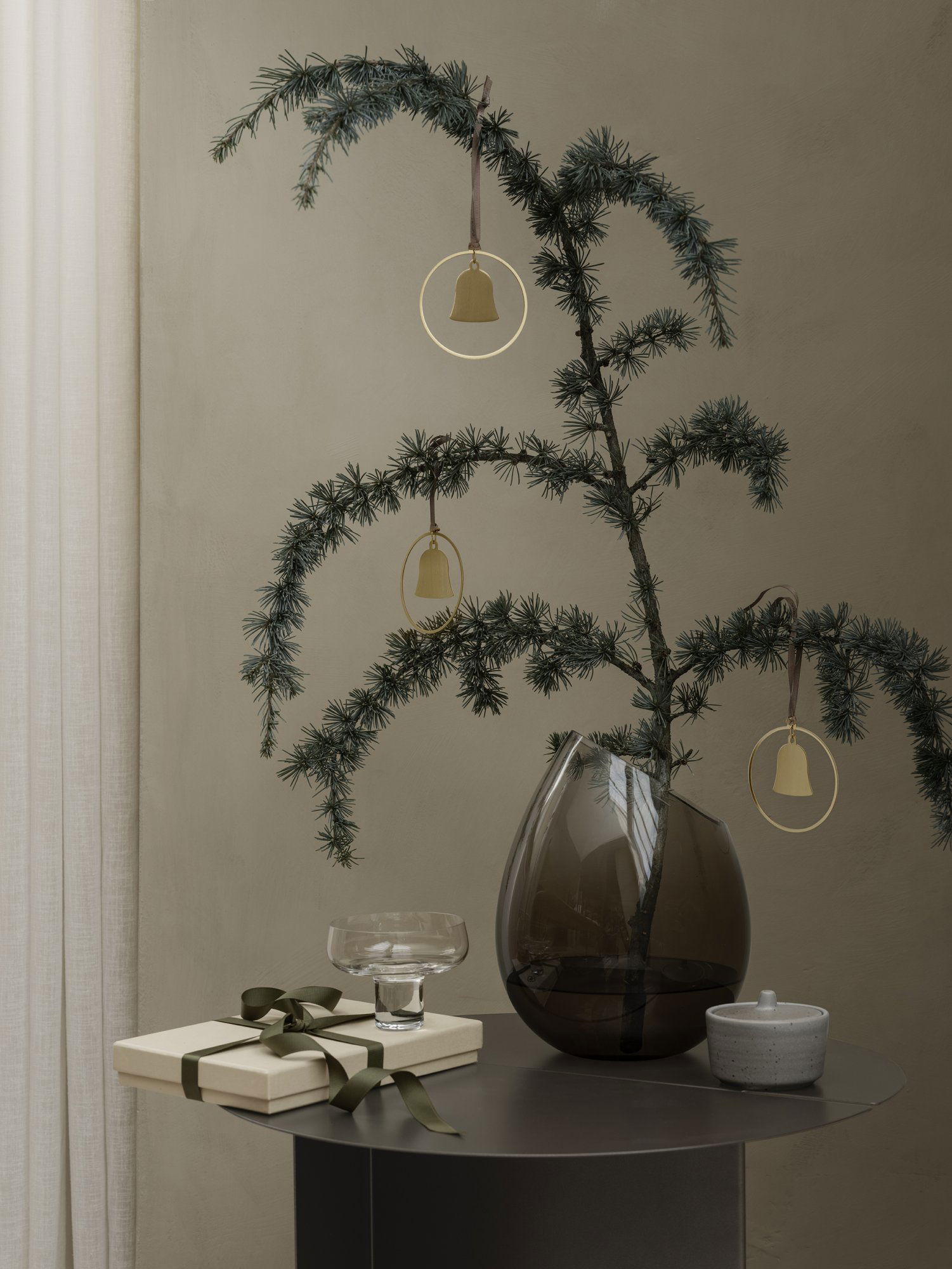 Elegante Weihnachtsdekoration mit einem grünen Baum, goldenen Glocken und einem Geschenk auf einem stilvollen Tisch.