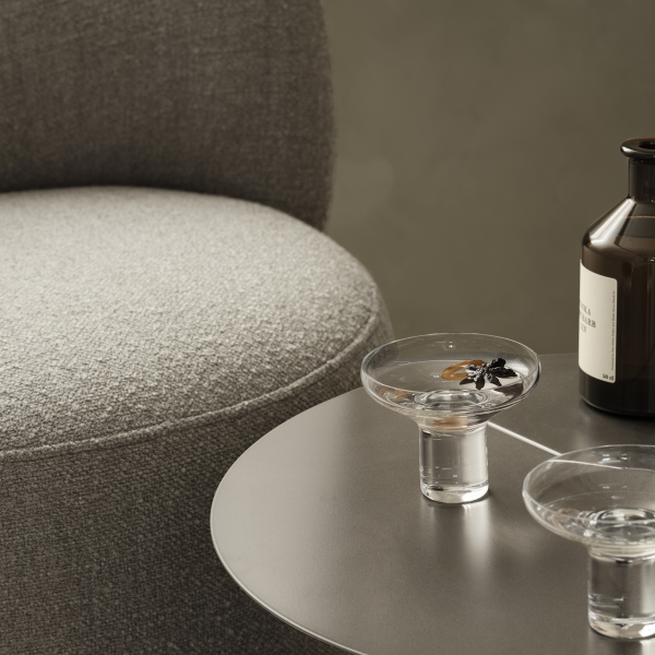 Stylisches Wohnzimmer-Setup mit einem grauen Stuhl, dekorativen Glas-Schalen und einer dunklen Flasche.