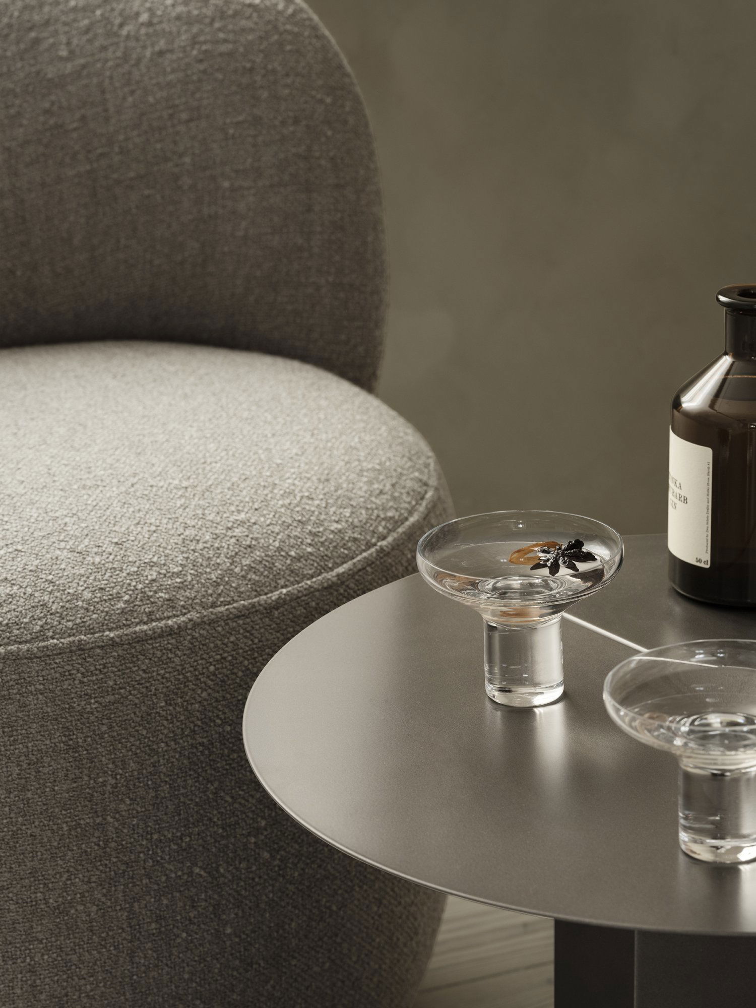 Stylisches Wohnzimmer-Setup mit einem grauen Stuhl, dekorativen Glas-Schalen und einer dunklen Flasche.