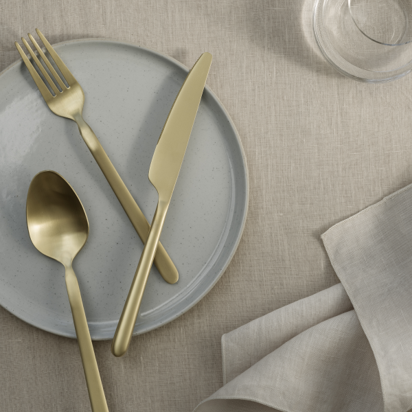 Elegantes goldenes Besteckset auf einer minimalistischen Tischdekoration mit einem grauen Teller und einer Leinenserviette.