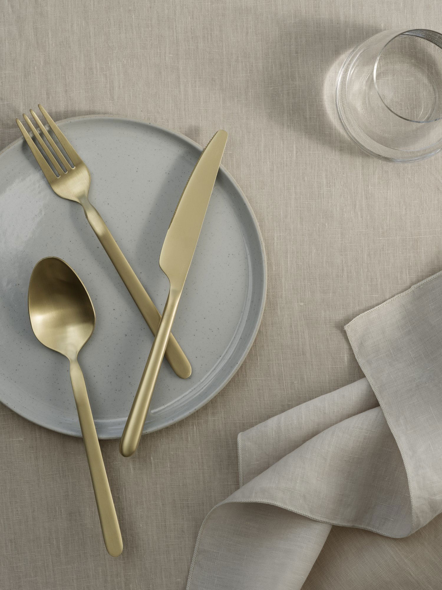 Elegantes goldenes Besteckset auf einer minimalistischen Tischdekoration mit einem grauen Teller und einer Leinenserviette.