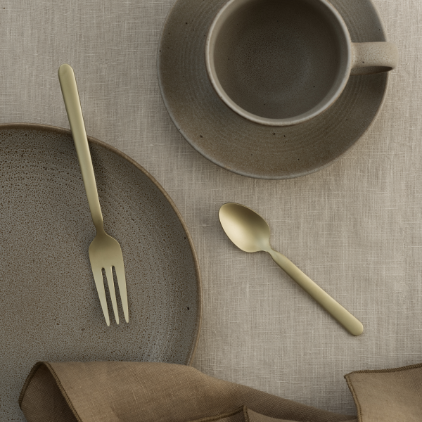 Elegant gold cutlery on a textured plate and rustic cup, set on a linen tablecloth.