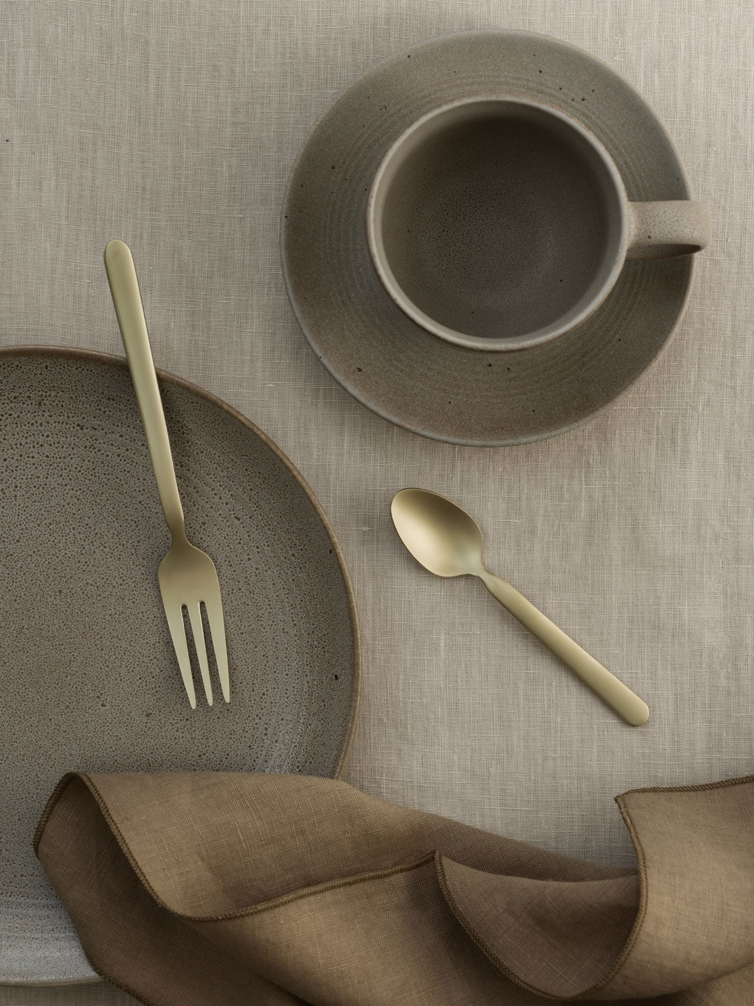 Elegant gold cutlery on a textured plate and rustic cup, set on a linen tablecloth.