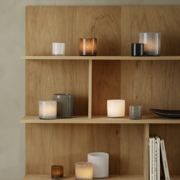 Verschiedene dekorative Kerzen auf Holzregalen vor einem neutralen Wandhintergrund.