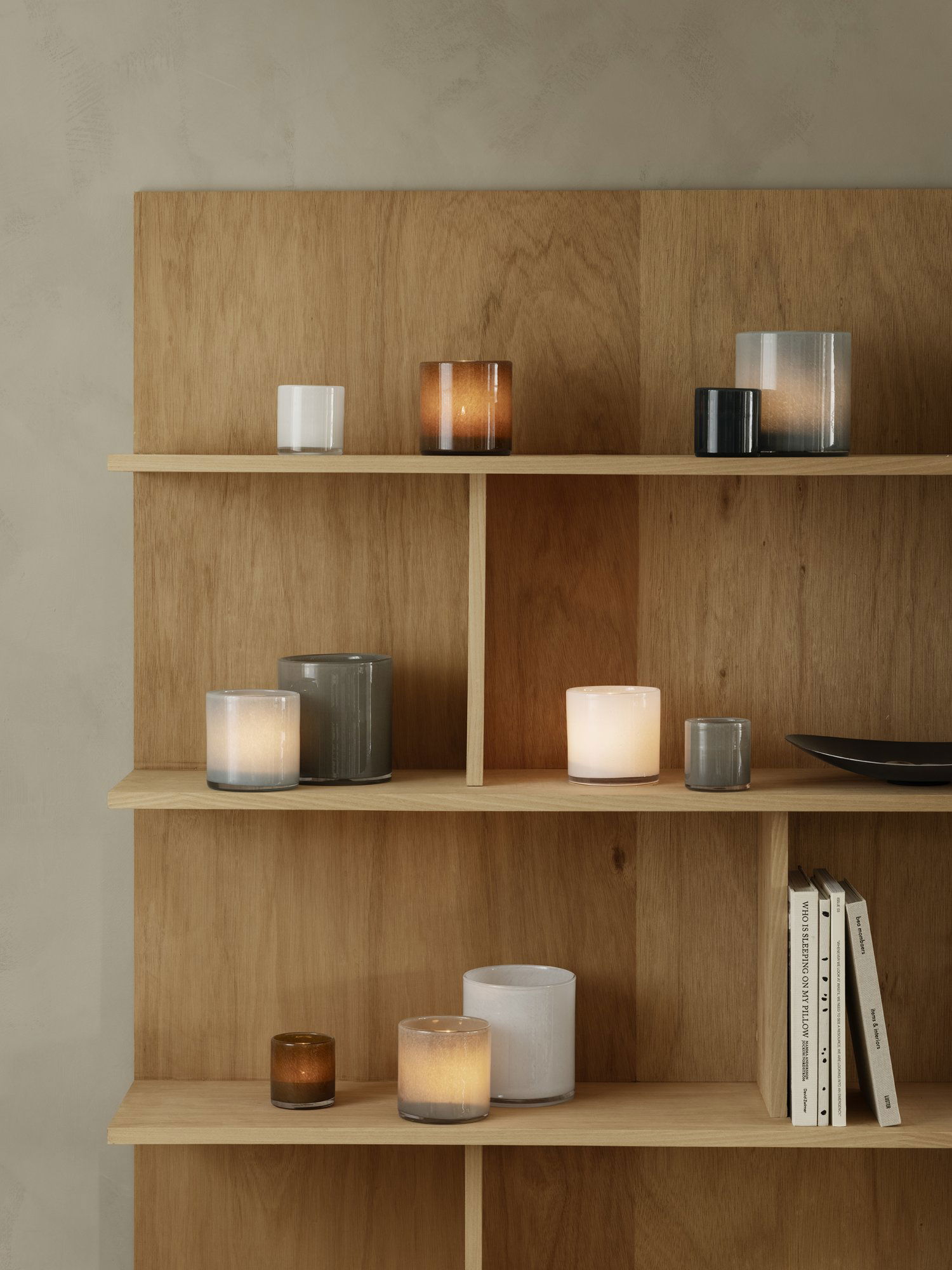 Verschiedene dekorative Kerzen auf Holzregalen vor einem neutralen Wandhintergrund.