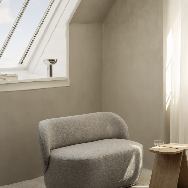 Gemütlicher, moderner Winkel mit einem grauen Stuhl und natürlichem Licht aus einem schrägen Fenster.