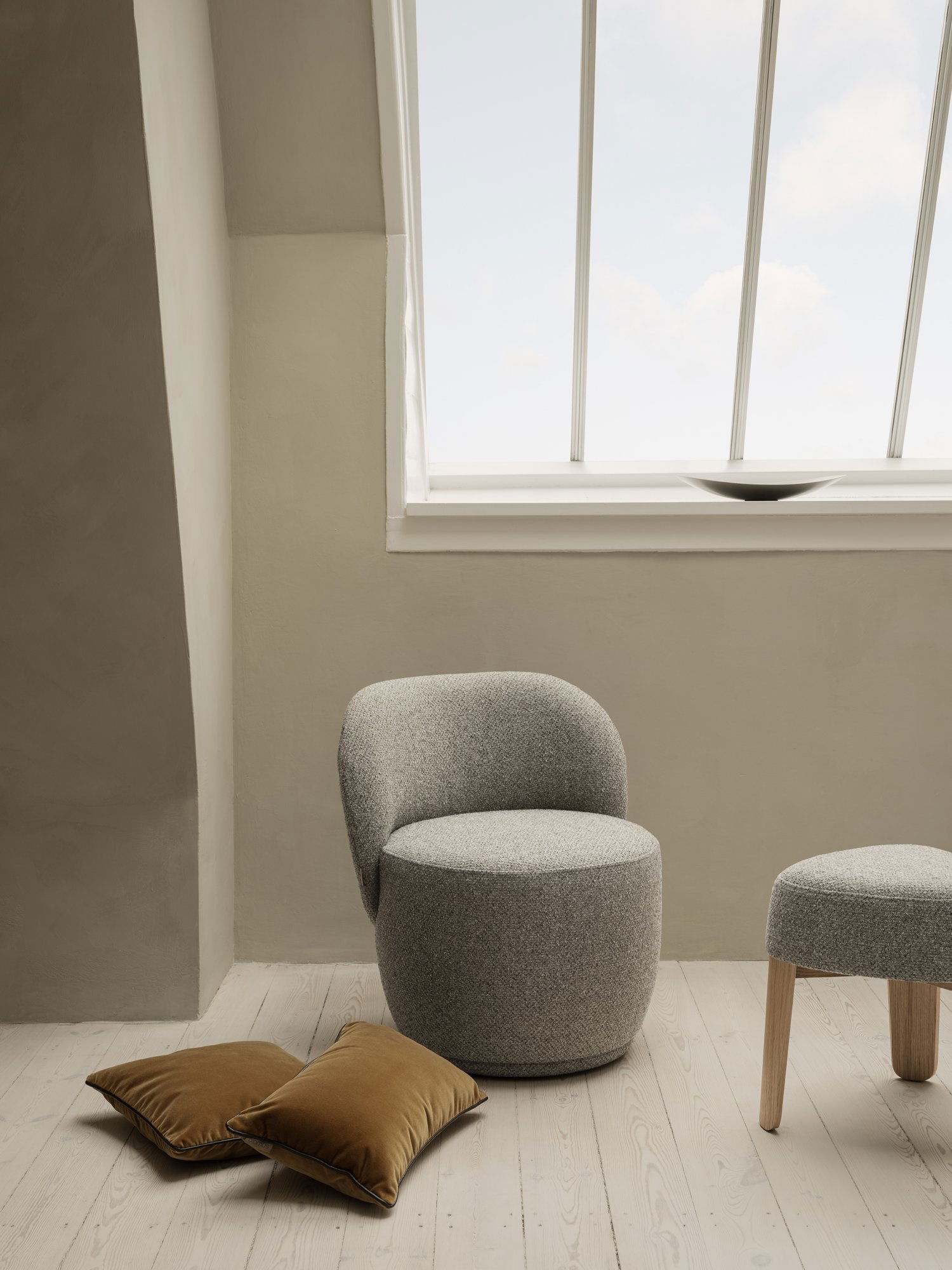 Gemütlicher moderner grauer Stuhl in einem minimalistischen Raum mit natürlichem Licht von einem großen Fenster.