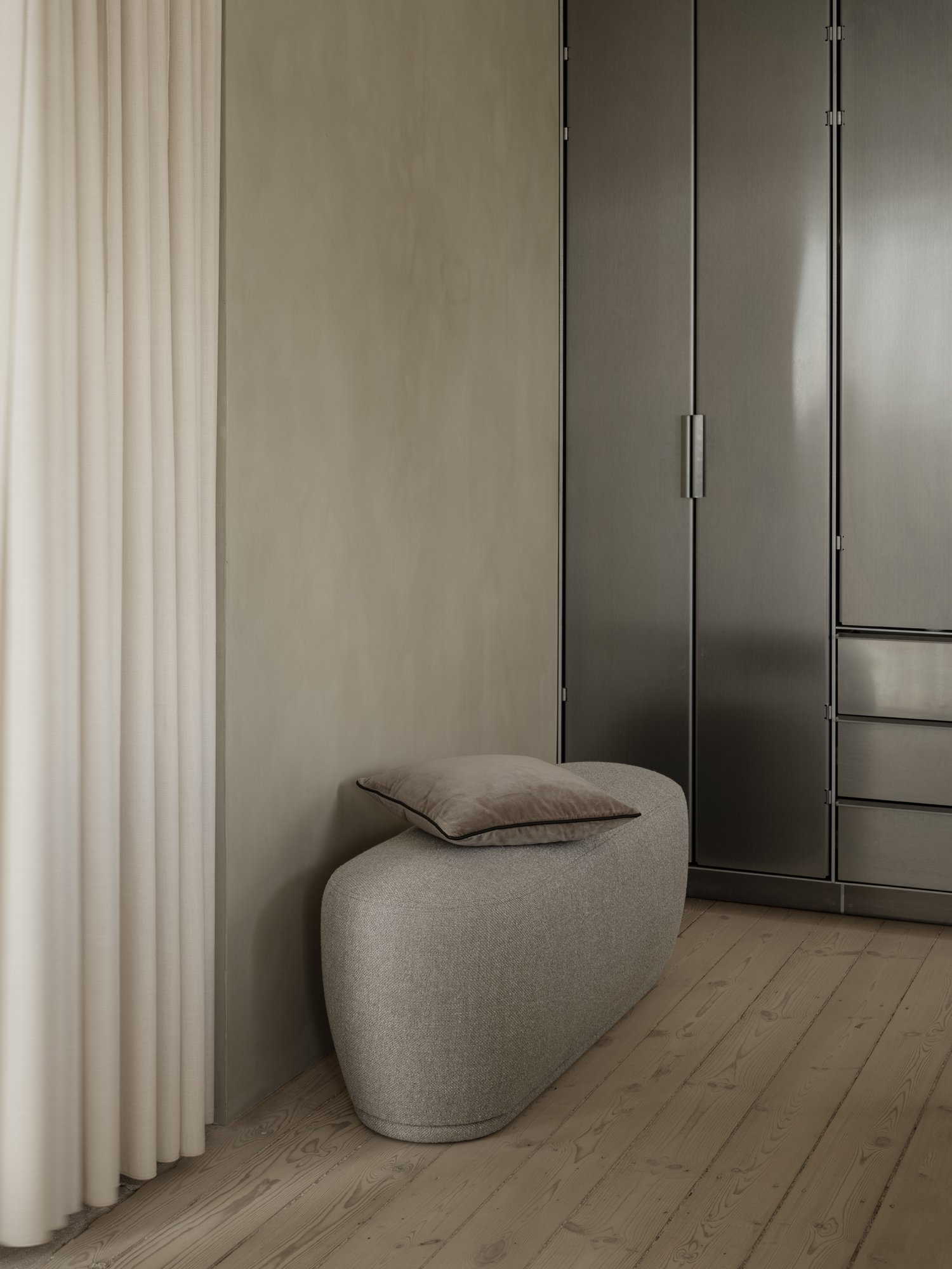 Moderner minimalistischer Innenraum mit einer weichen grauen Bank vor einem eleganten metallischen Kleiderschrank.