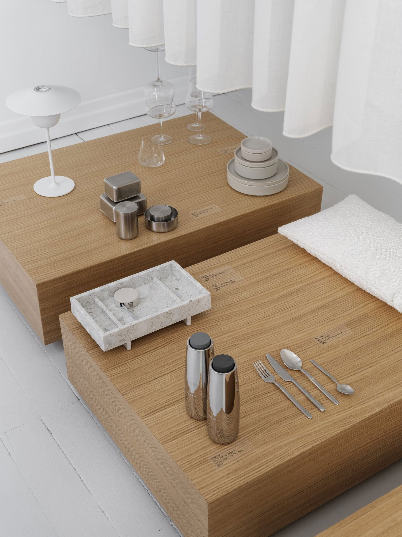 Modern minimalist dining setup with wooden tables and elegant tableware in soft lighting.