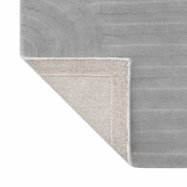Weicher grauer Teppich in der Ecke mit strukturiertem Design und eingefassten Kanten für moderne Dekoration.