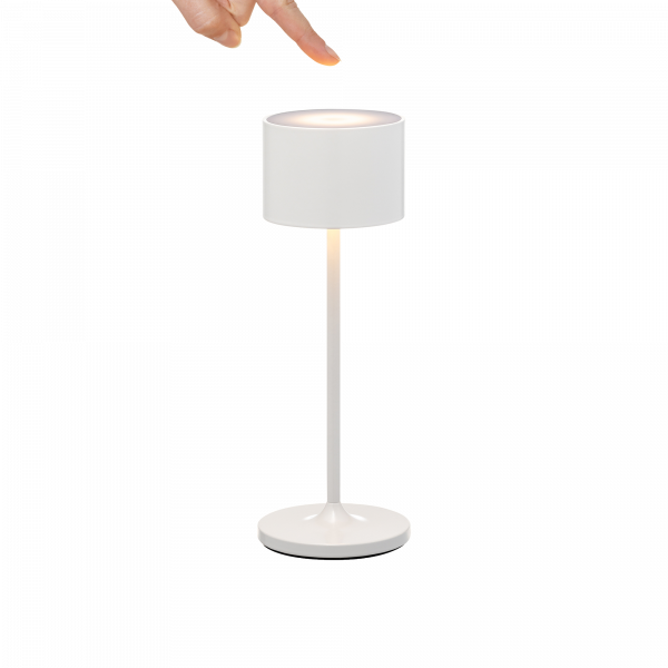 Hand zeigt auf eine moderne weiße Tischlampe mit einem zylindrischen Schirm und einem eleganten Design.