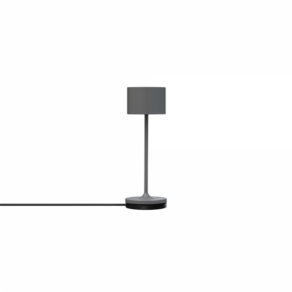Minimalistische graue Tischlampe mit einem zylindrischen Schirm und schwarzem Kabel auf einem weißen Hintergrund.
