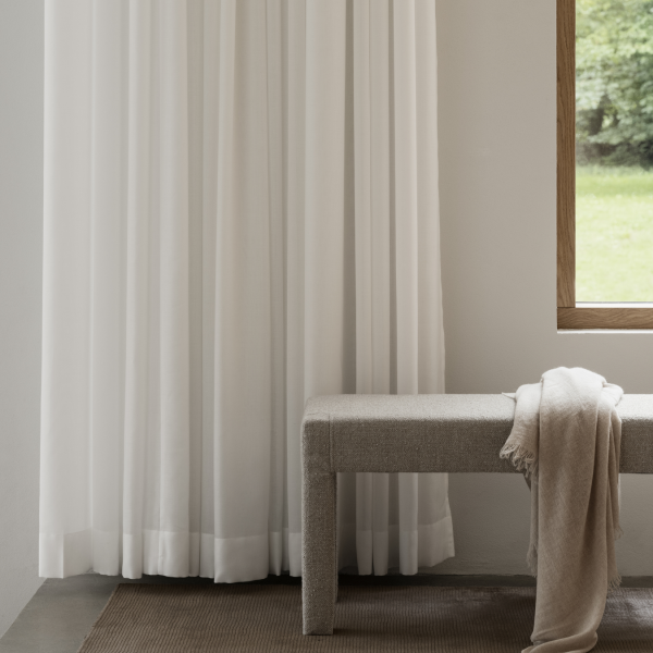 Elegant white curtains drape beside a cozy bench in a softly lit, modern interior.