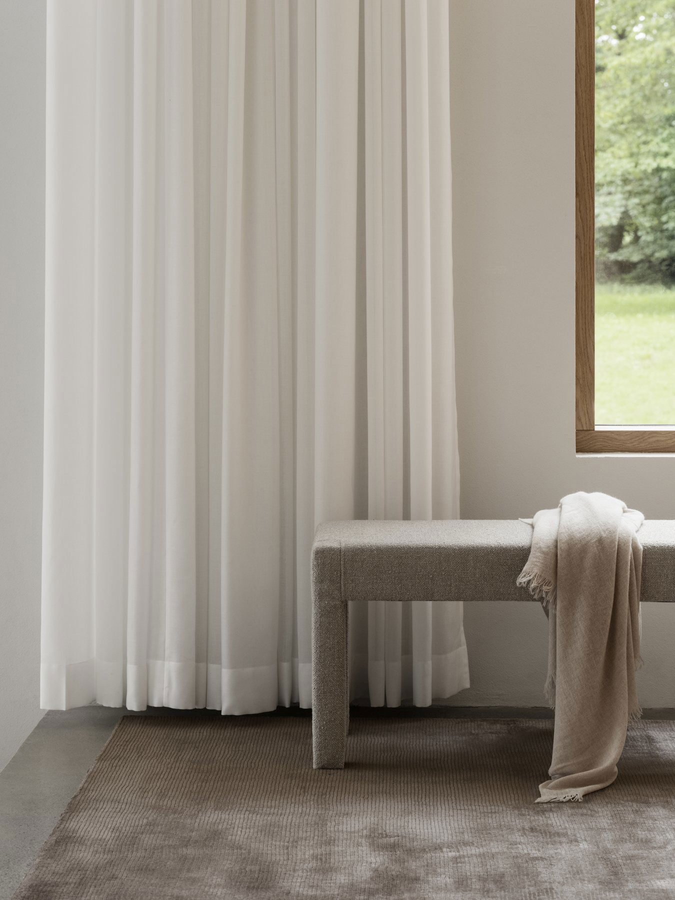 Elegant white curtains drape beside a cozy bench in a softly lit, modern interior.