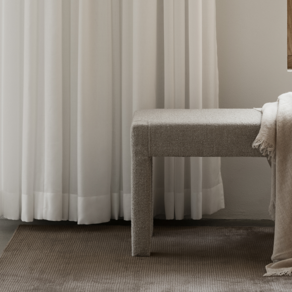Cozy interior featuring a textured bench beside flowing white curtains and a soft blanket.